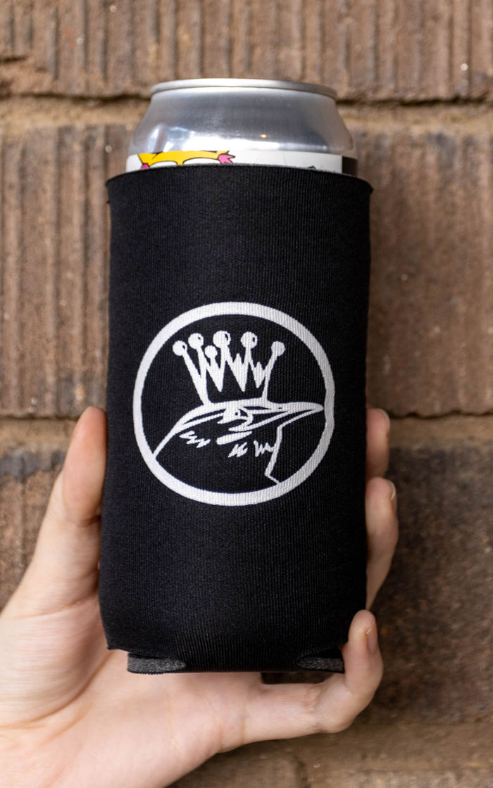 A hand holding a black Wren House koozie printed with the crown-and-bird logo